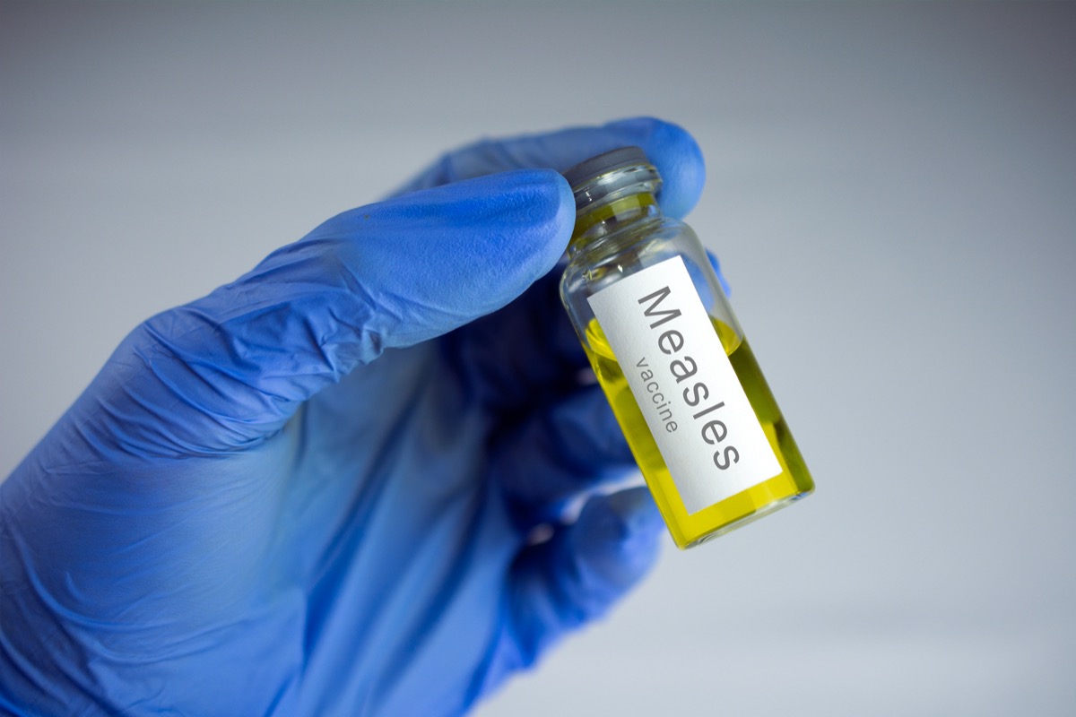 Hands in blue gloves holding a jar with a yellow vaccine