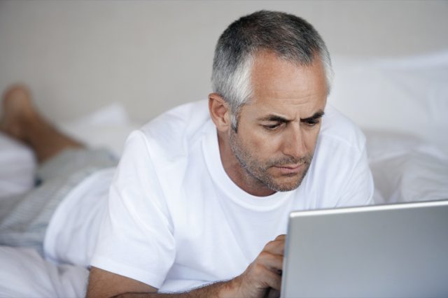 Middle aged man using laptop while lying in bed