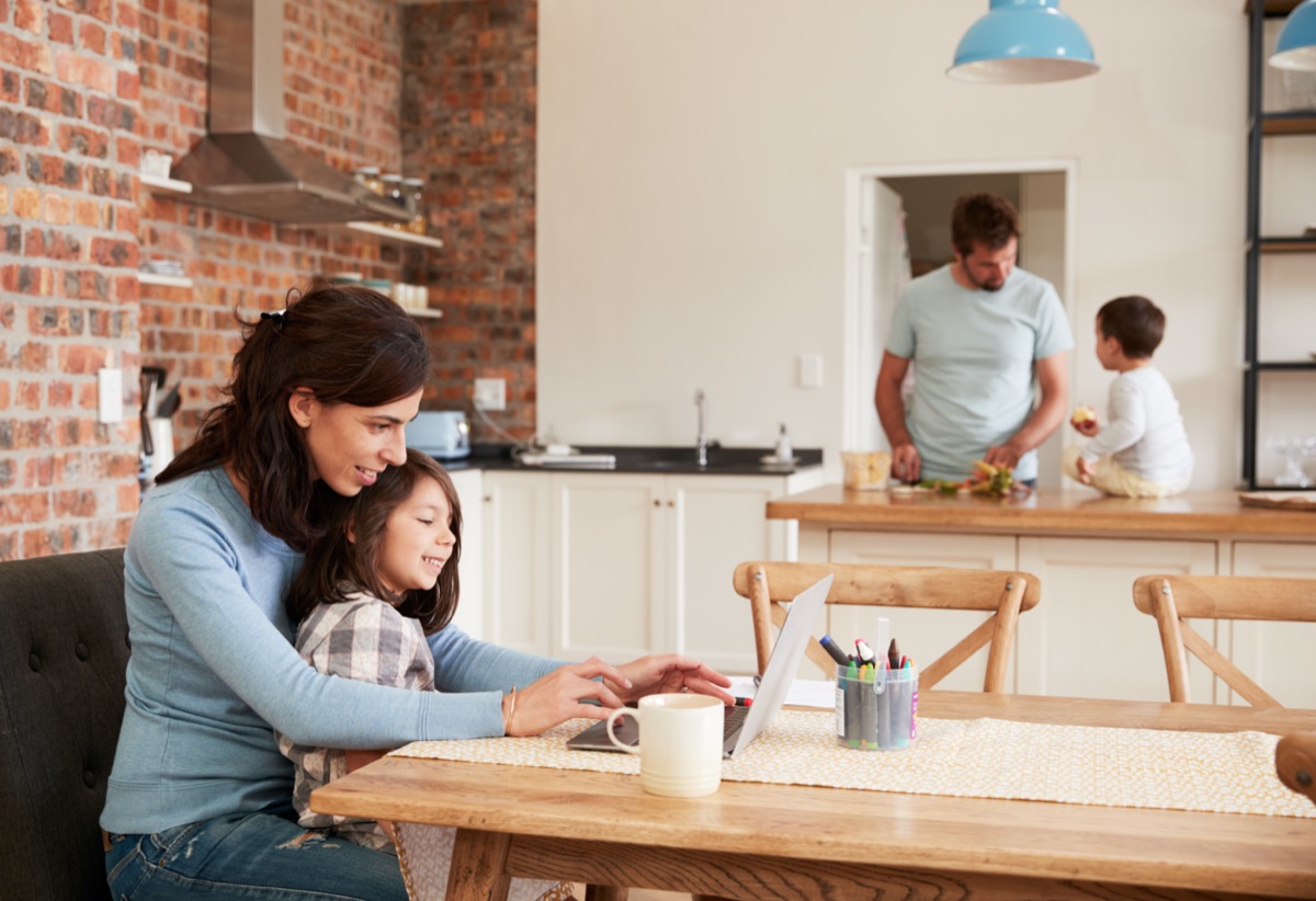 Busy Family Home With Mother Working As Father Prepares Meal