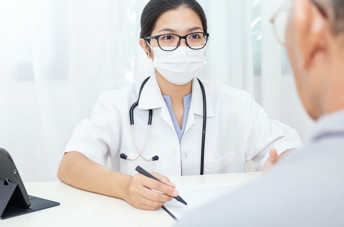 Portrait of asian woman doctor wear protection face mask showing a patient some information on digital tablet clip board, patient listen to specialist doctor in clinic office