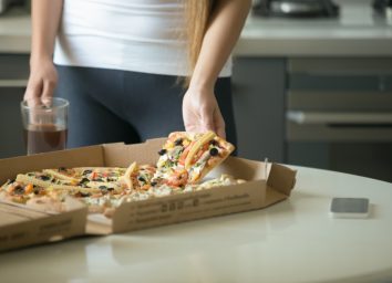 Female hands taking a slice of pizza from the box on the kitchen table, close up