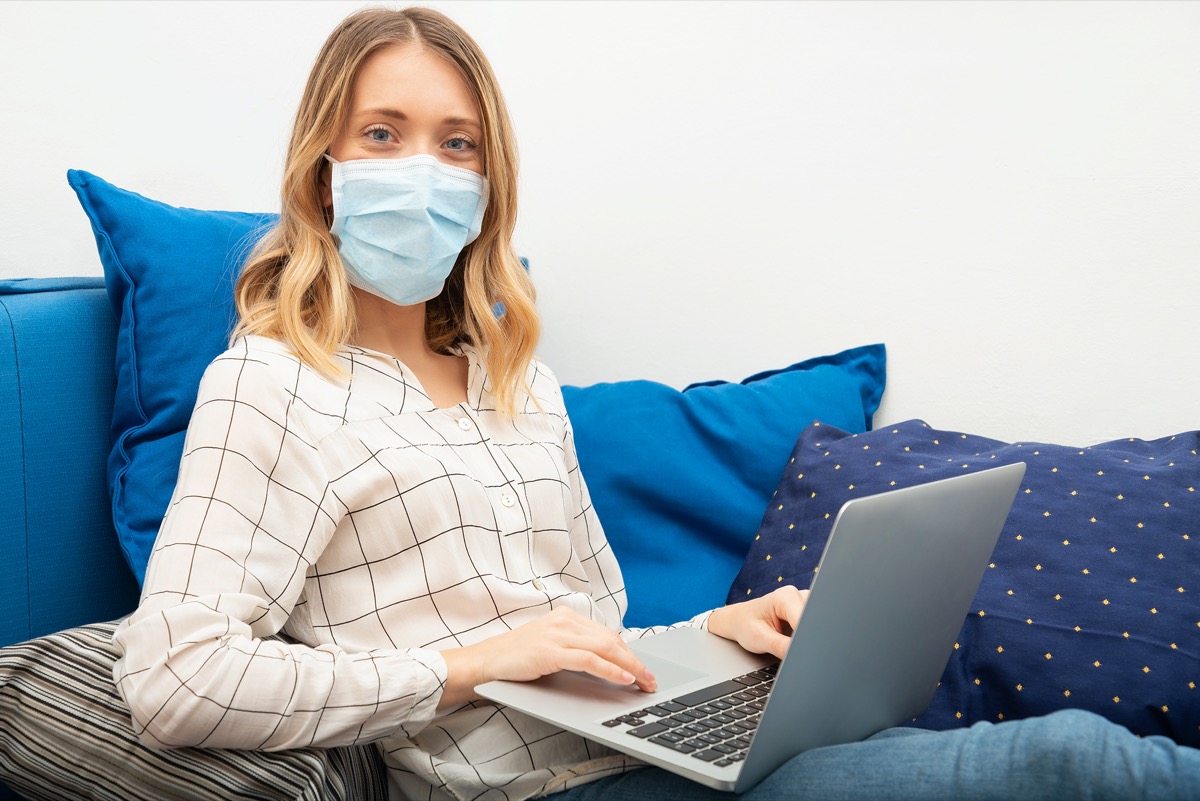 Young business woman working from home with laptop, wearing protective mask