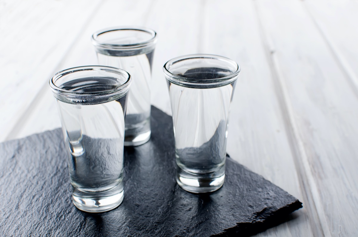 three Vodka shots with ice on black stone board on white wooden table, copy space
