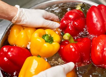 Man wearing gloves washing peppers vegetables produce in large bowl water