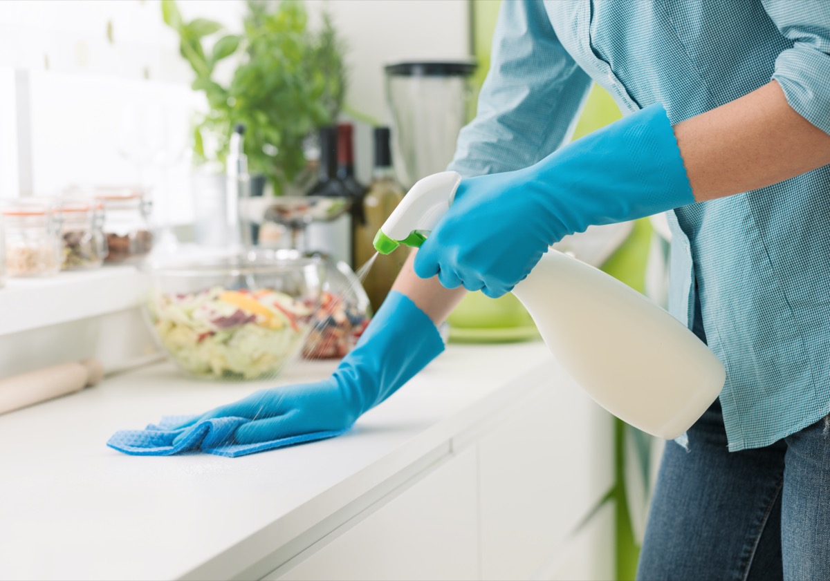 Woman cleaning and polishing the kitchen worktop with a spray detergent, housekeeping and hygiene
