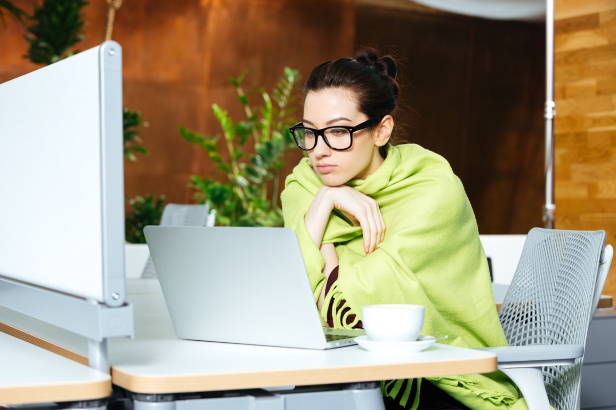 woman coveted with coverlet using laptop and feeling cold on workplace