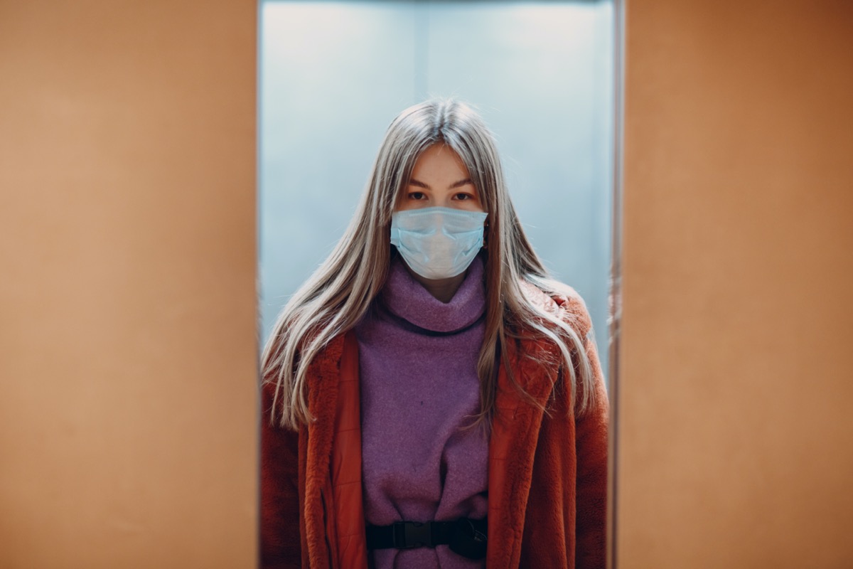 Young chinese woman standing in elevator in medical mask. Doors are closing. Coronavirus COVID-19 pandemic concept.