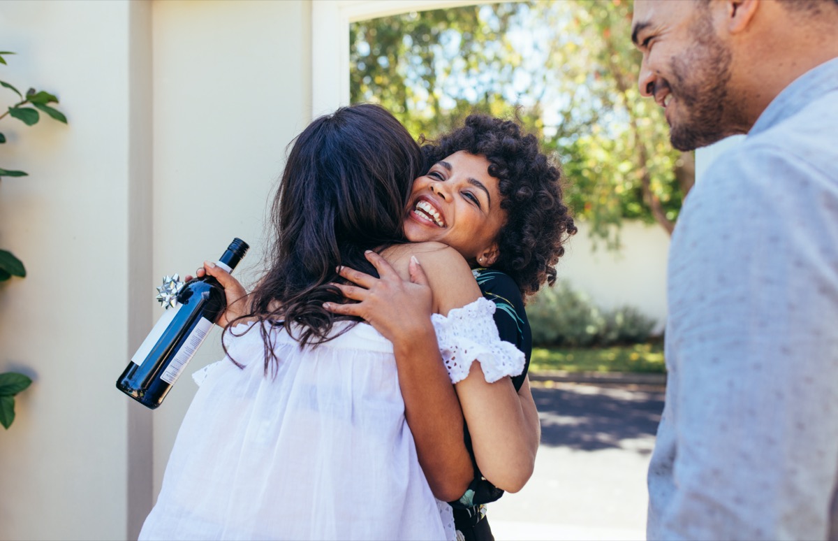 Woman greeting couple for having a new house. Smiling young woman with wine bottle congratulating her friend