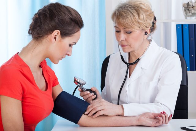 Doctor taking blood pressure of female patient at office