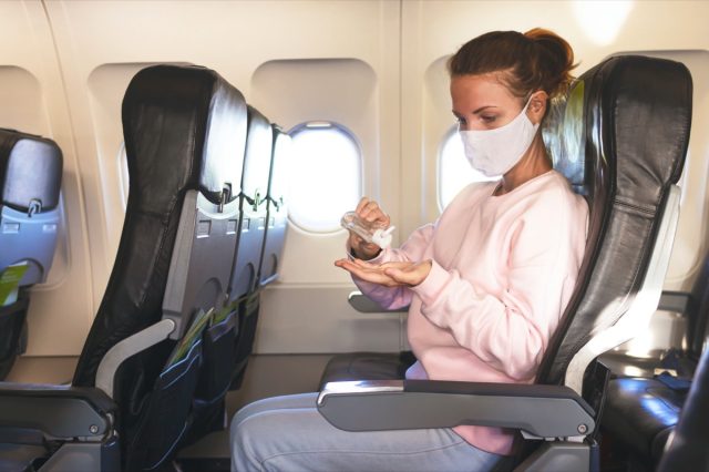 woman in airplane disinfects hands with gel, sanitizer during flight