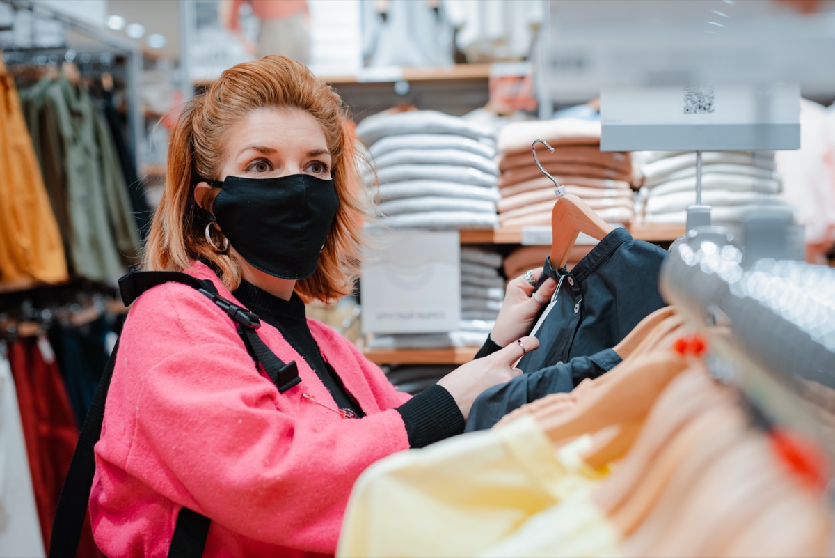 woman with phone bright pink shopping Mall coat with black protective mask on her face from virus infected air. concept of virus protection in the fashion, beauty, and shopping industries