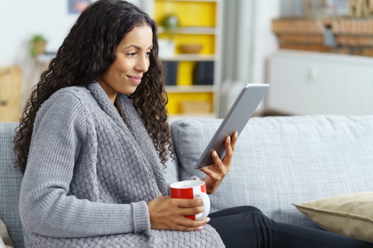 woman reading on tablet at home with a cup of coffee in her hand