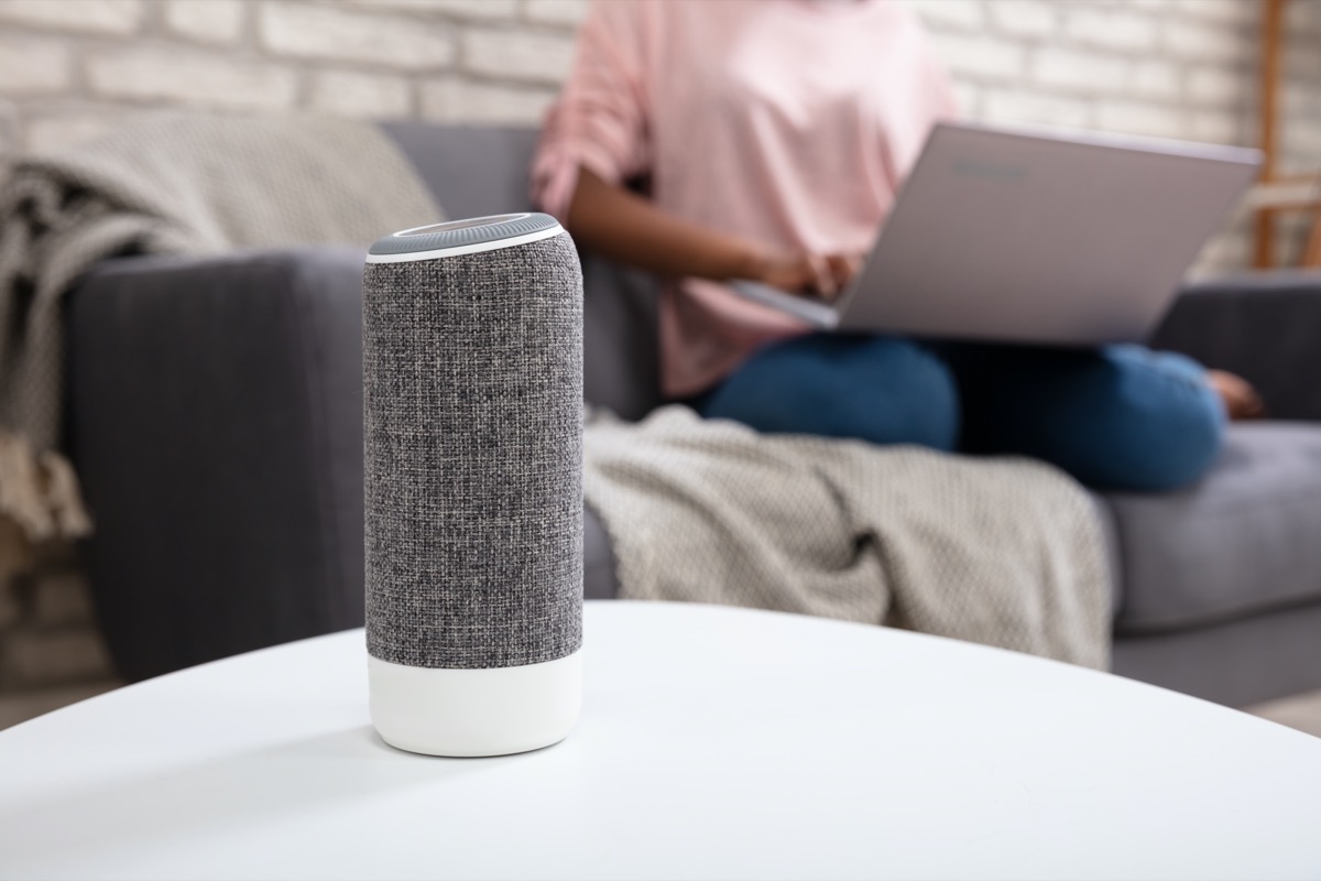Woman With Laptop Using Voice Assistant Speaker At Home
