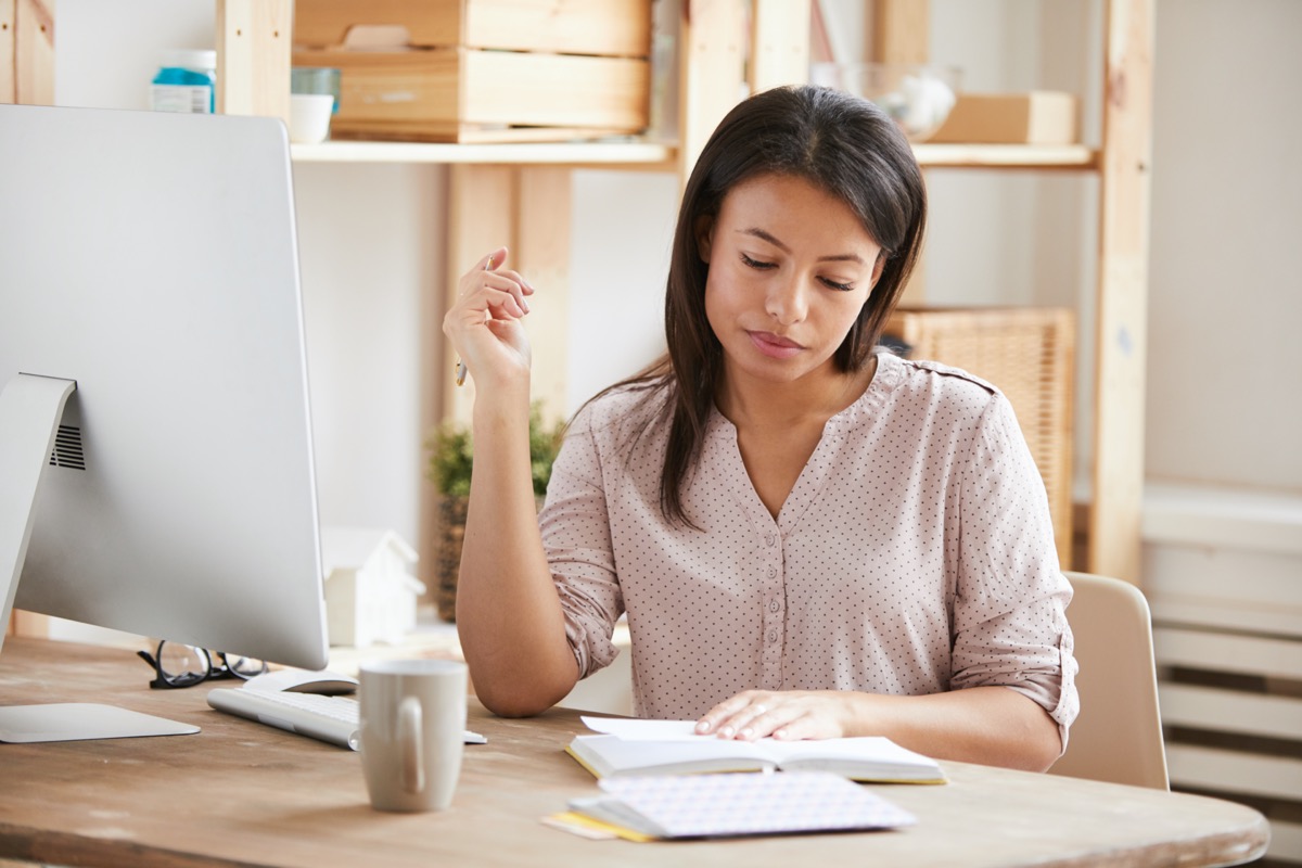 Portrait of beautiful Mixed race woman writing in notebook while sitting at desk in office, copy space