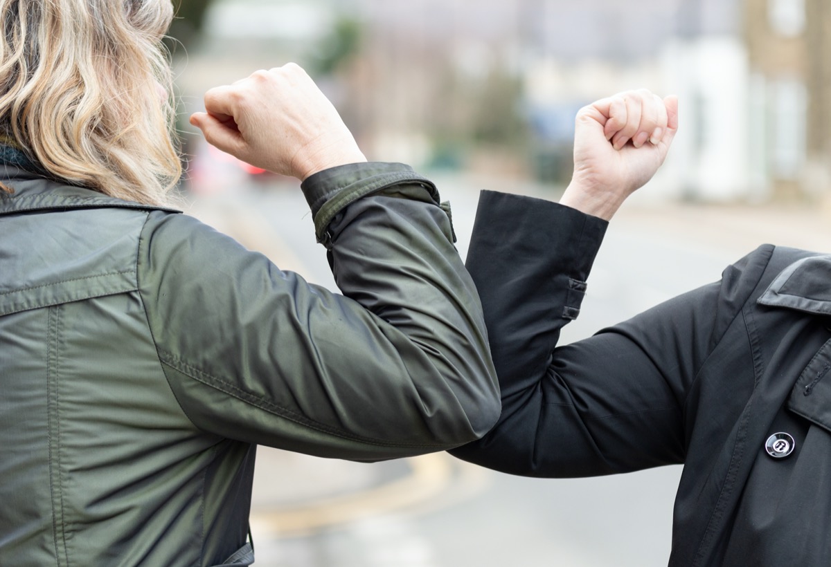 Two women friends meet in a street with bare hands. Instead of greeting with a hug or handshake, they bump elbows instead