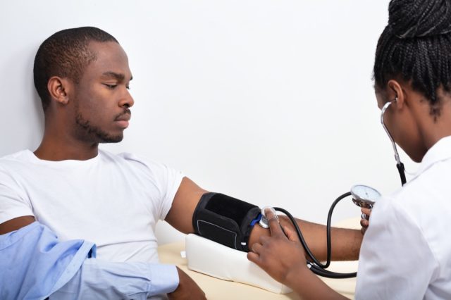 Doctor's Hand Measuring Blood Pressure Of Male Patient.