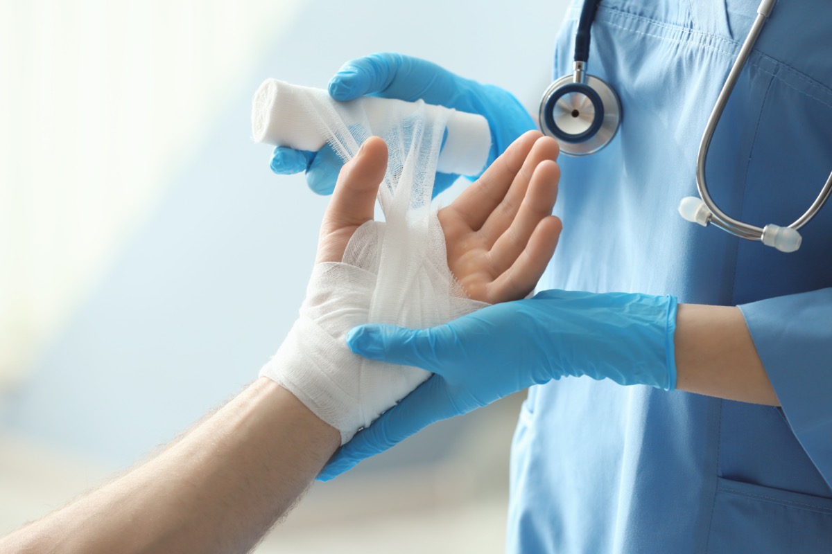 Medical assistant applying bandage onto patient's hand in clinic