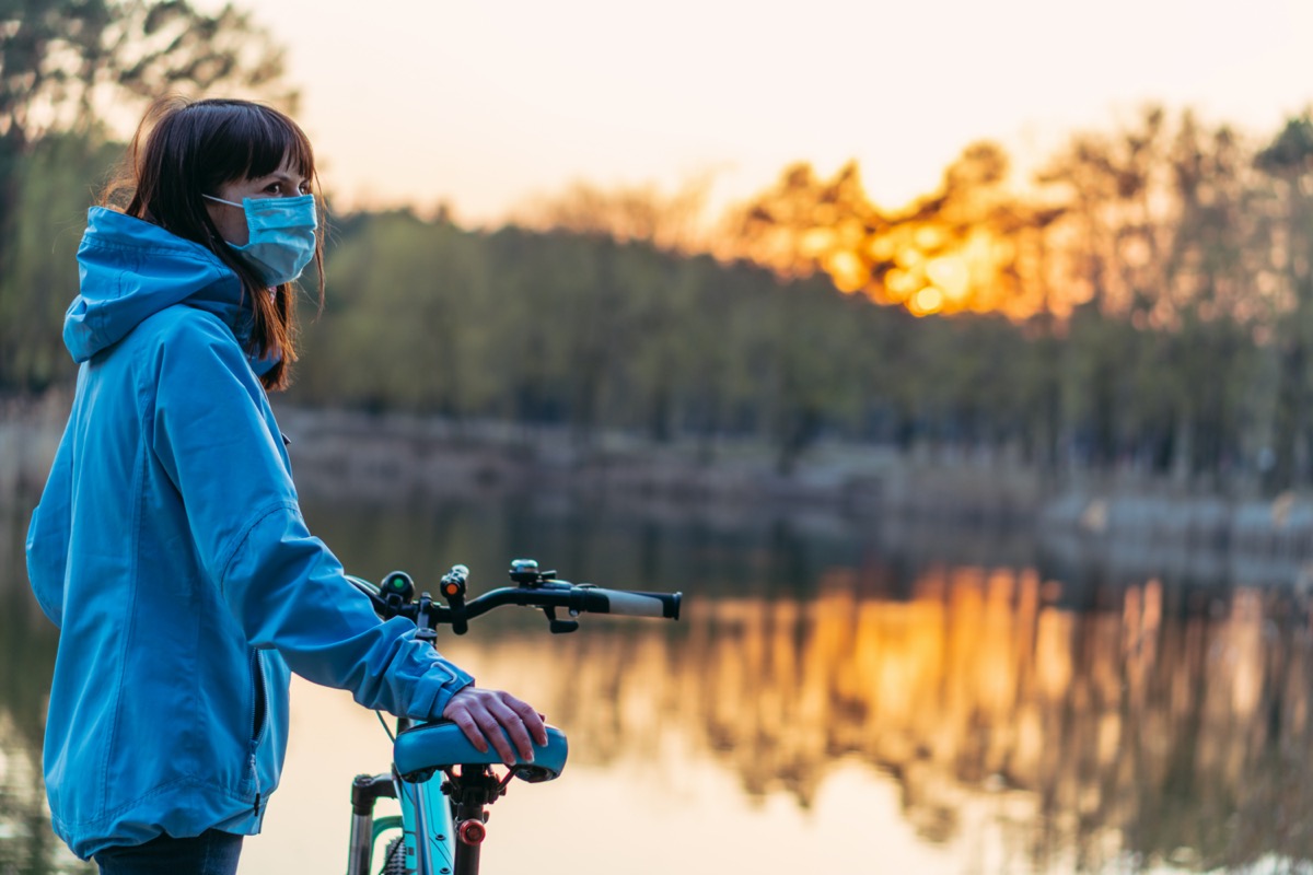 Virus. A woman with a bicycle and a protective medical mask is standing in the park.