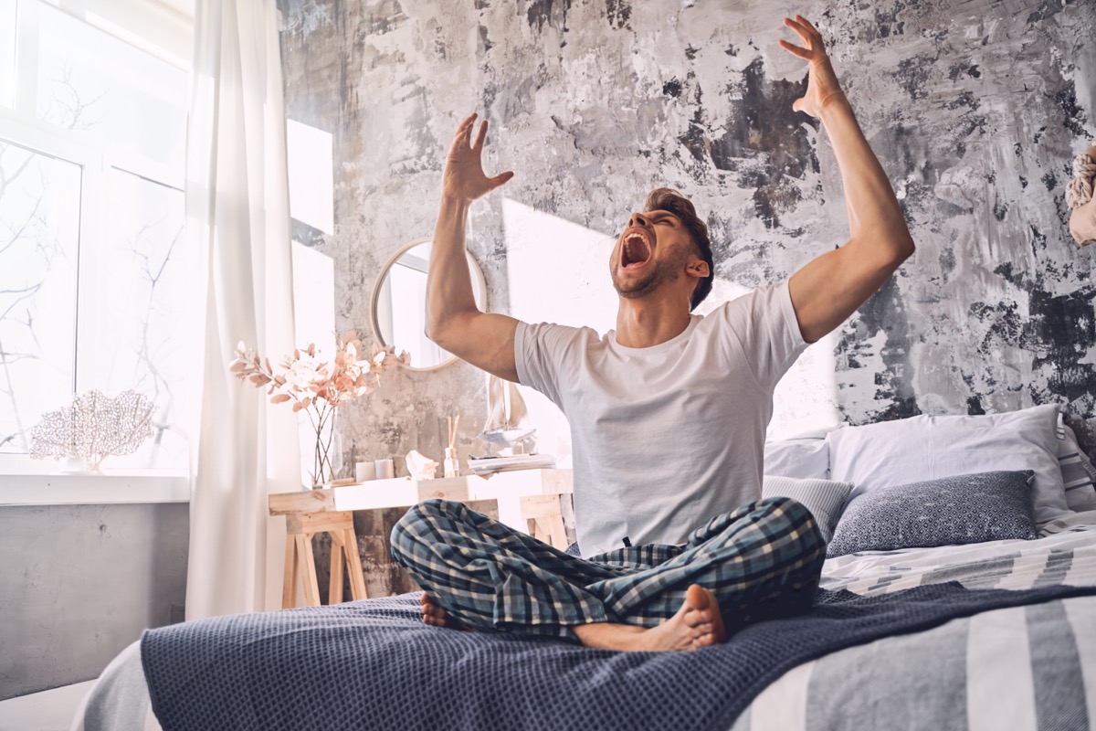 Irritated man crossing legs while sitting on the bed and shouting at home