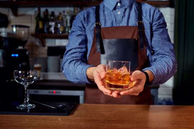 Hands of a bartender at bar restaurant with glass whiskey drink