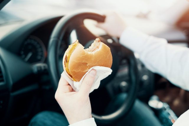 A man eats a hamburger and drives sitting in his car
