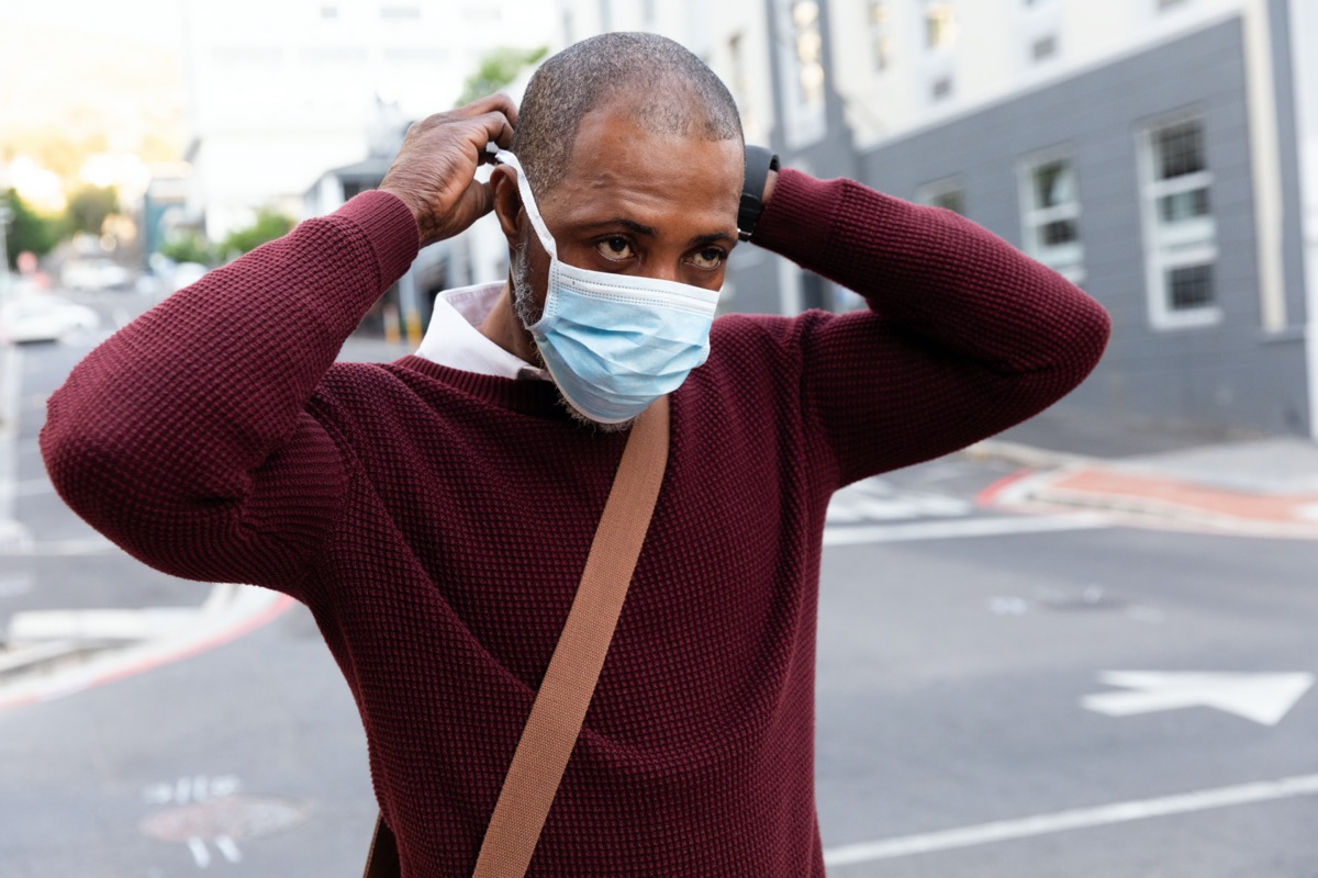 African American man wearing red pullover, out and about in the city streets during the day, putting on a face mask against air pollution and covid19 coronavirus.