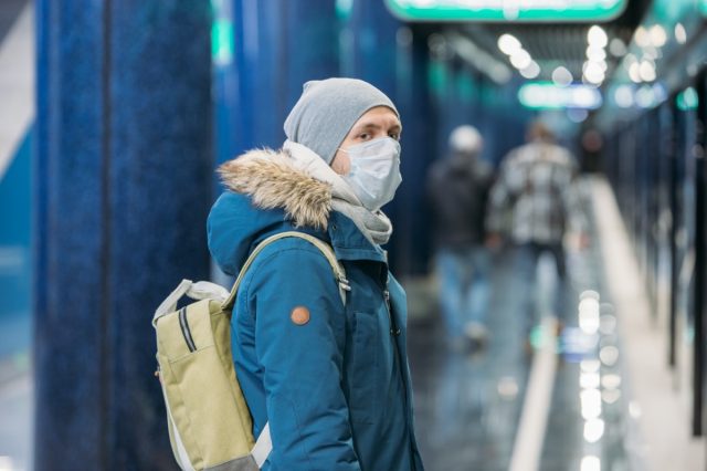 Ill young man feeling sick, wearing protective mask against transmissible infectious diseases and as protection against the flu in public and transportation.