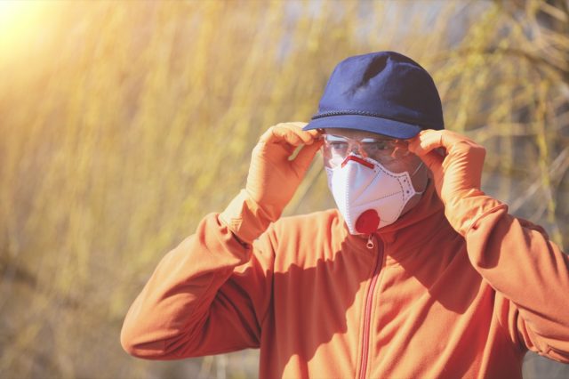 A man in medical face mask (respirator) and safety glasses outdoors