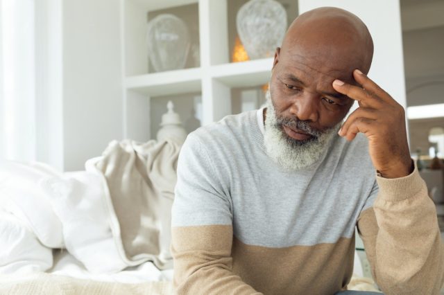 senior African American man sitting on white sofa in light room in beach house