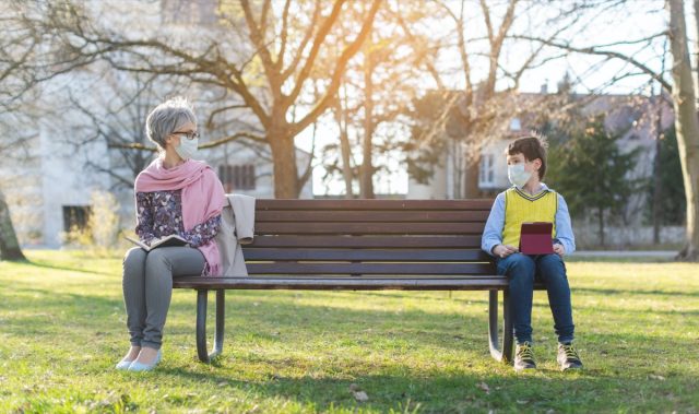 Grandmother and grandson separated by social distancing on park bench