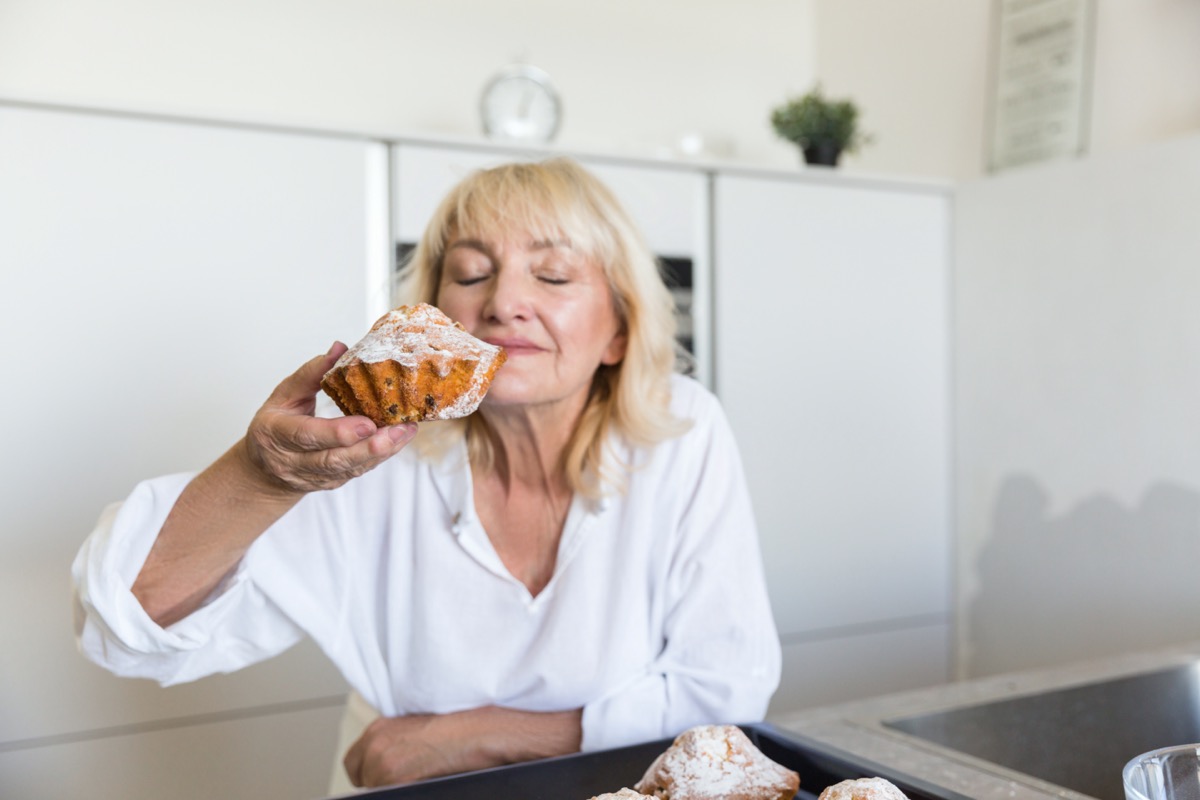 Senior woman smelling the taste of her homemade muffins while standing on a kitchen