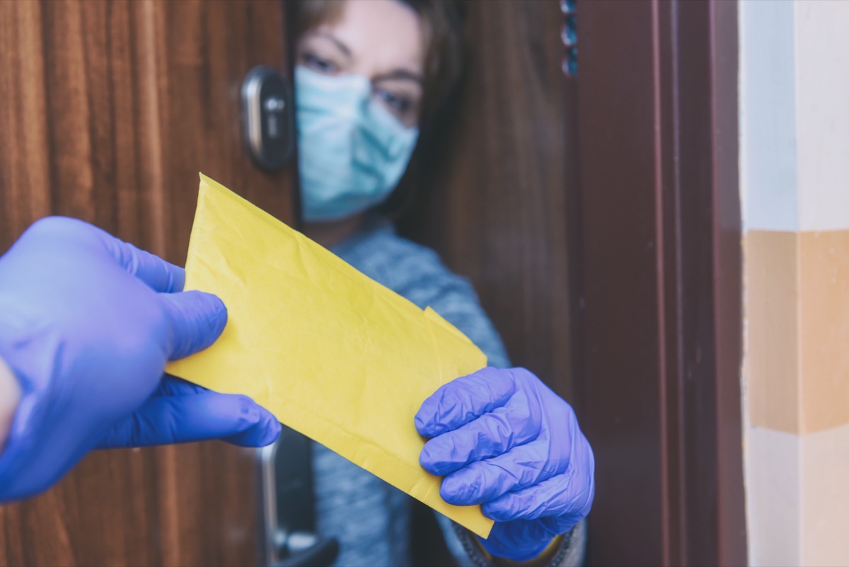 Woman wearing a protective face mask and gloves opening the door and receiving a mail post letter; epidemic of corona virus covid-19