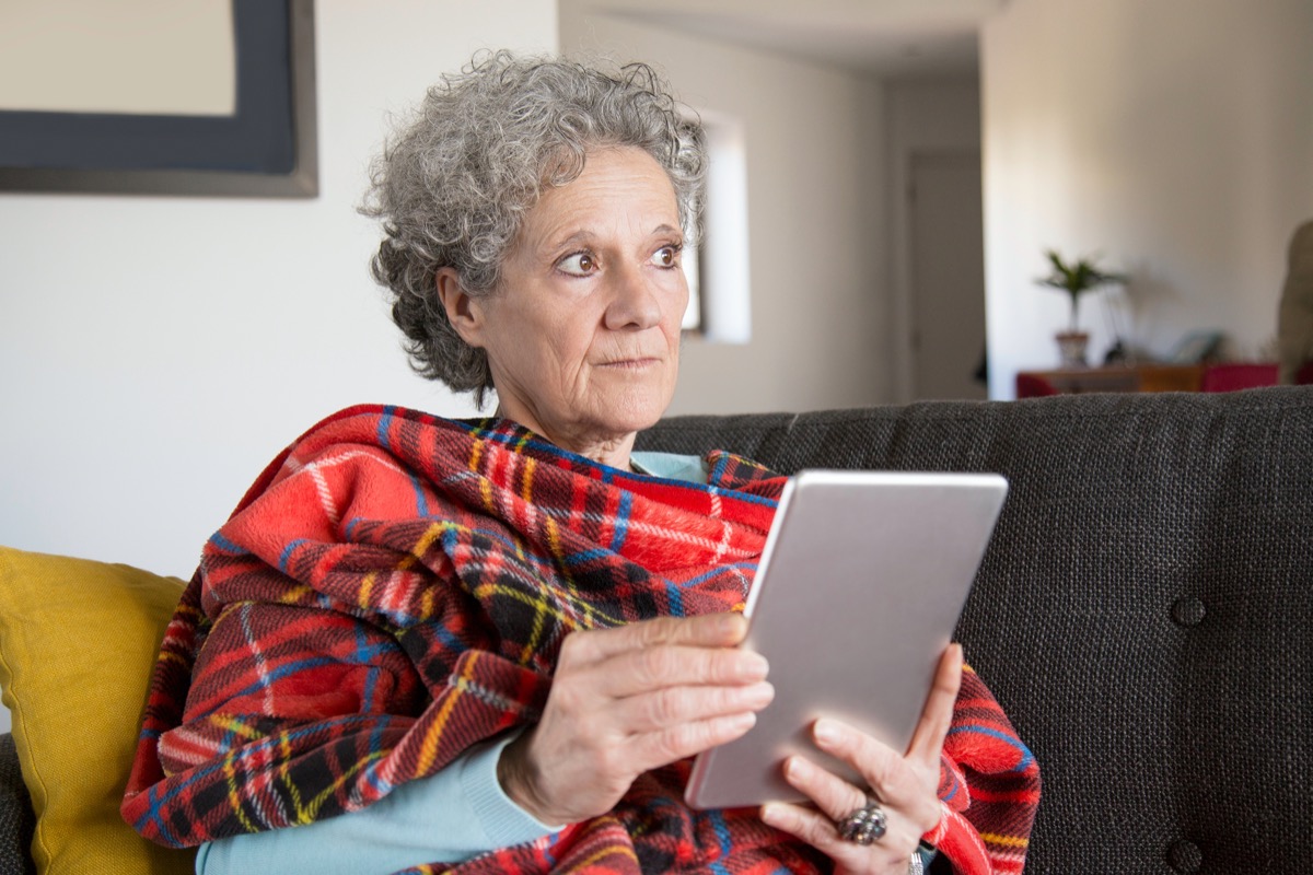 Pensive frowning senior woman reading online book on tablet at home