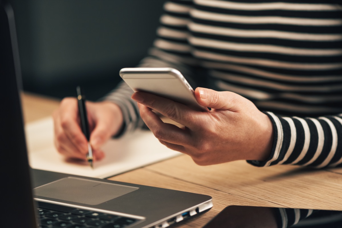 Woman writing contact list from mobile phone into her business agenda notebook for backup