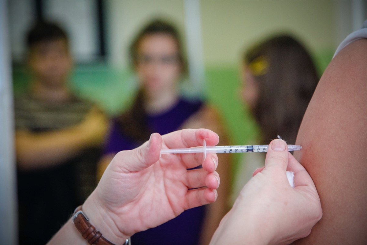 Nurse administering vaccination to students arms in a high school.