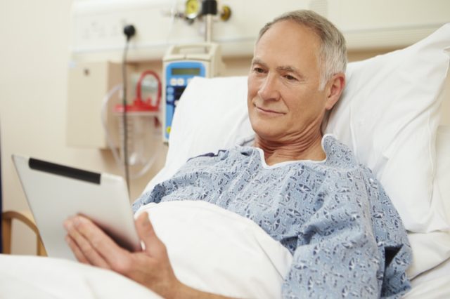 Senior Male Patient Using Digital Tablet In Hospital Bed