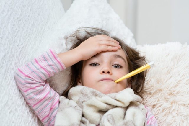 sick girl lying in bed with a thermometer in mouth and touch his forehead