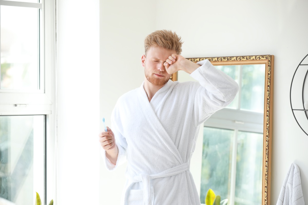 Morning of sleepy young man with toothbrush in bathroom