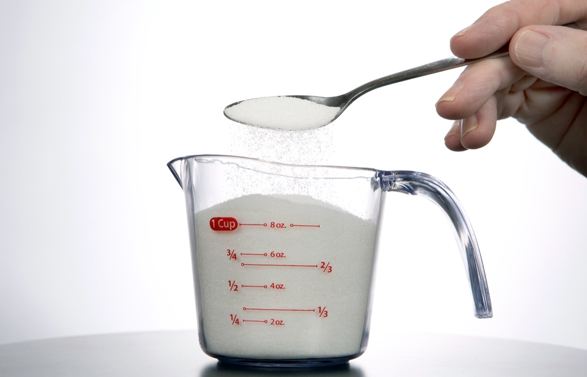 Man pours a spoonful of sugar into a measuring cup.