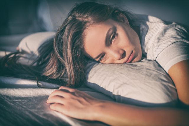 A tired woman lying in bed cannot sleep late at night due to insomnia