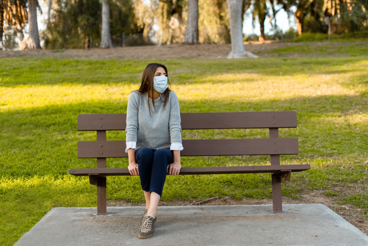 woman outdoor wearing medical face mask, social distancing, sitting on a bench, isolated from other people