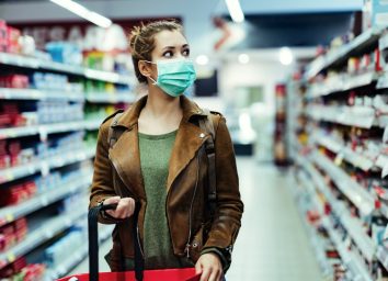 Young woman with face mask walking through grocery store during COVID-19 pandemic.