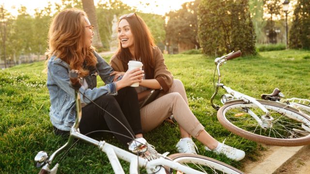 Image of two young beautiful women friends outdoors with bicycles in park.