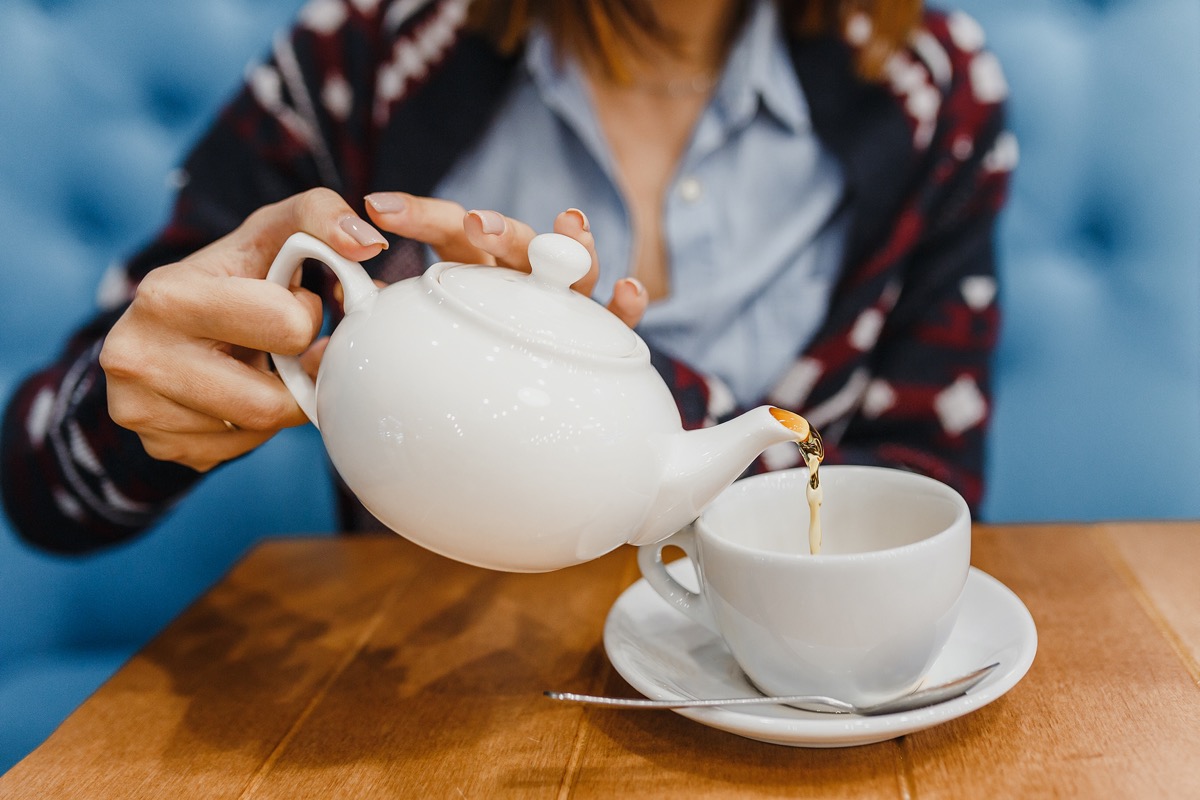 A person pours tea from a teapot nearby
