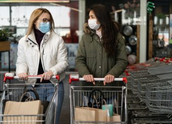 Two women in a medical mask enter a modern grocery market, a store. Coronavirus protection, quarantine, self-isolation.