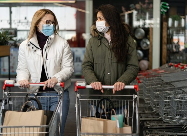 Two women in a medical mask enter a modern grocery market, a store. Coronavirus protection, quarantine, self-isolation.