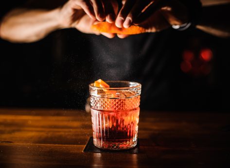 Bartender squeezing orange peel cocktail