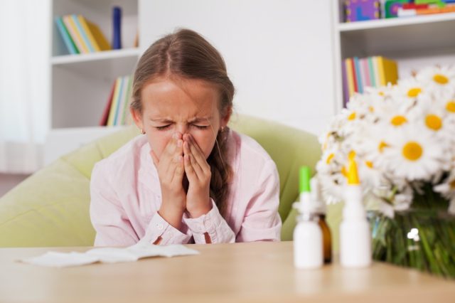 Young girl sneezing at home with paper towel prepared to blow her noise