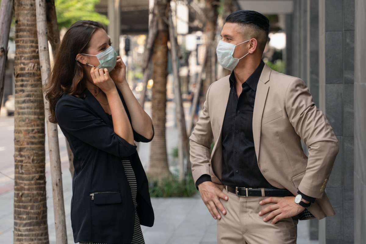 people wearing medical mask for coronavirus covid 19 protection standing together beside office building and talking in city