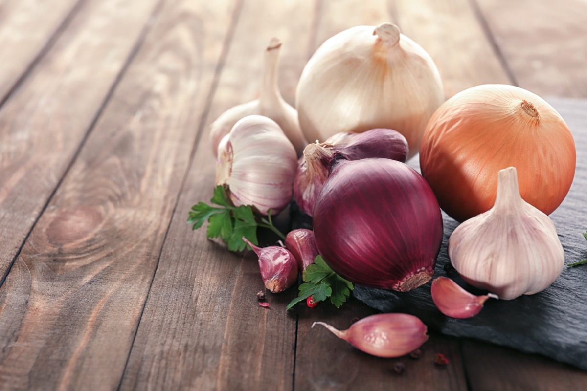 Slate plate with fresh garlic and onion on wooden table.